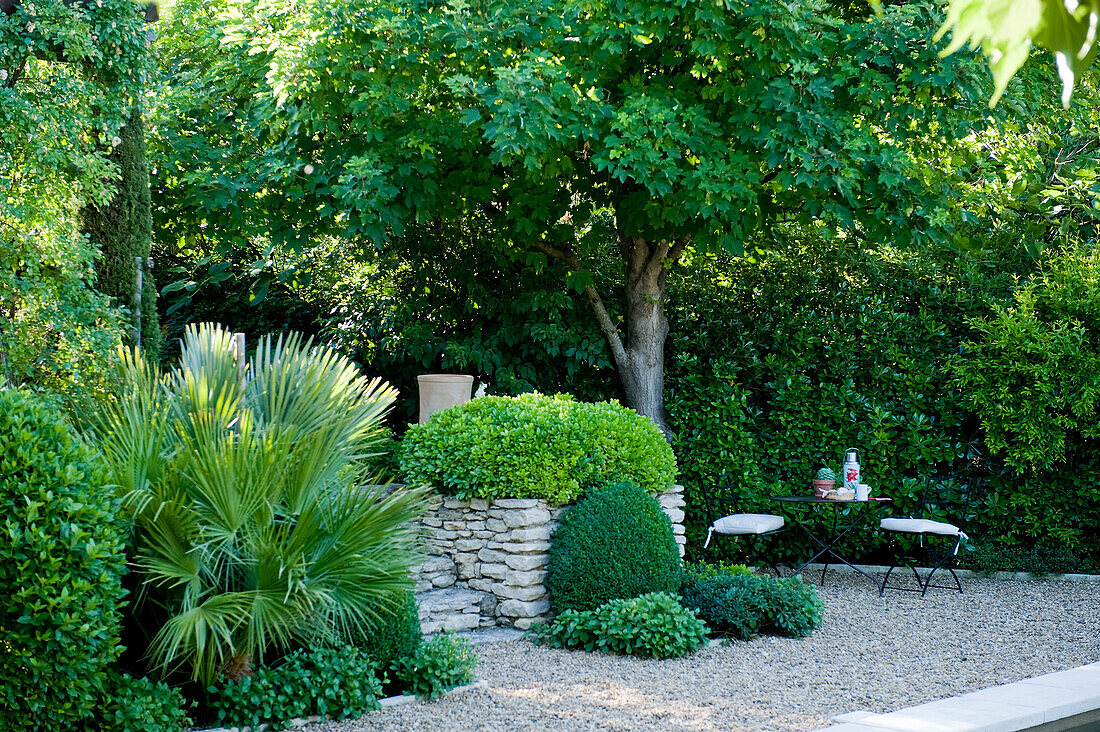 Seating area with round metal tables in the shady garden with gravel path