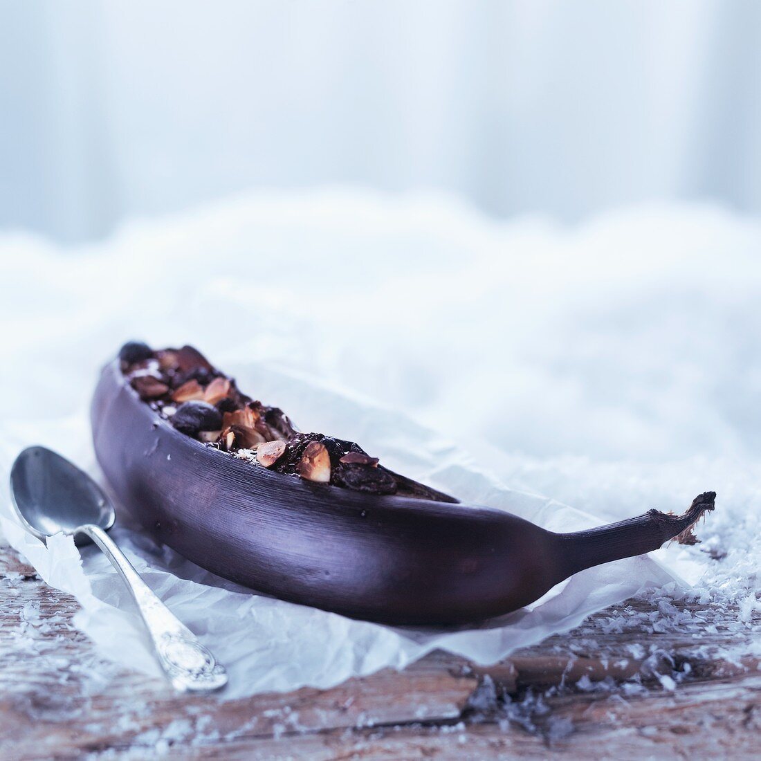 A banana baked in its skin topped with nuts and chocolate