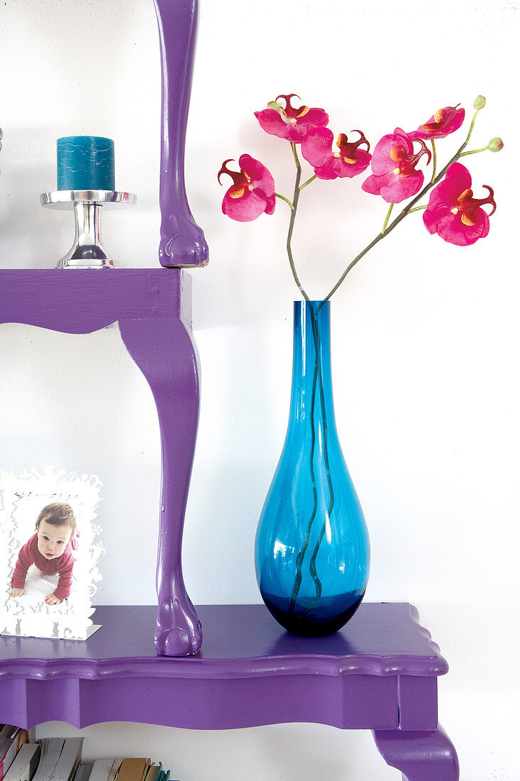 Orchideen in blauer Glasvase auf gestapelten, lila lackierten Tischhälften im Antikstil