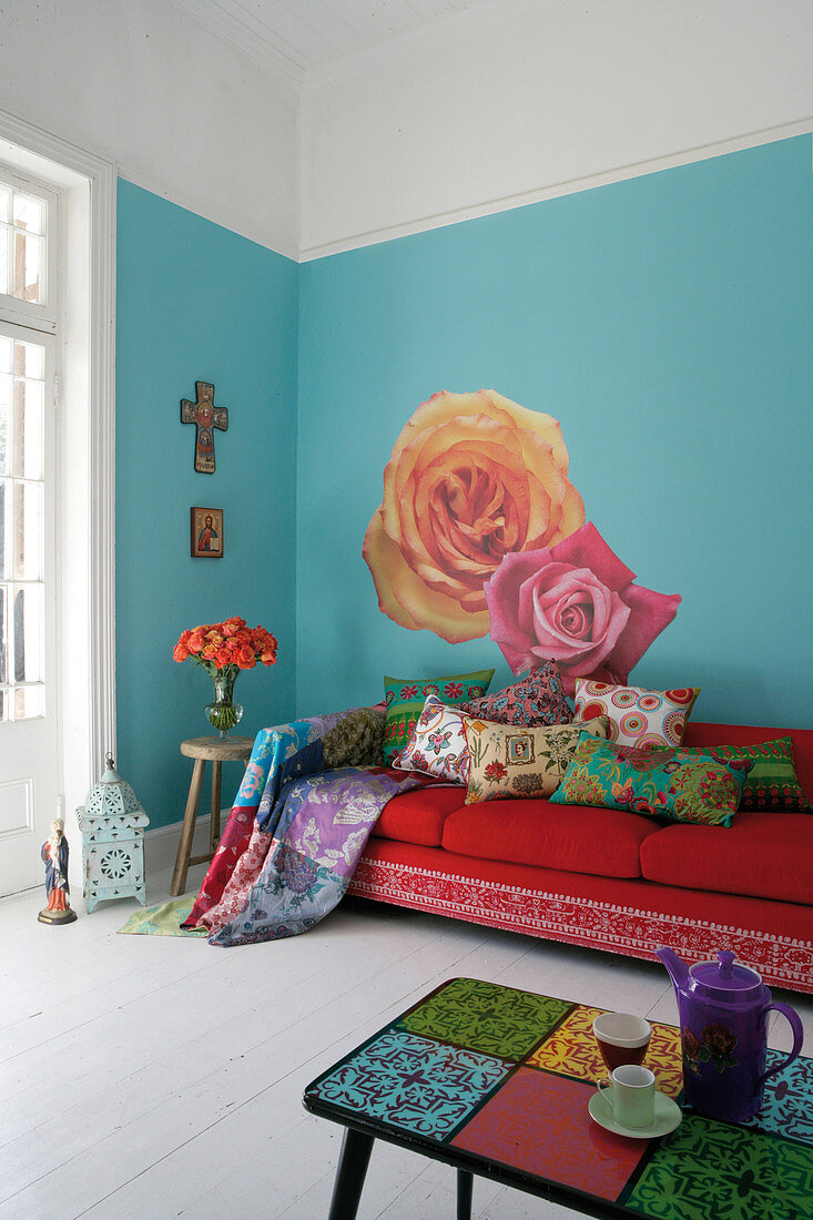 Mediterranean living room with sofa and colourful cushions against wall painted light blue with large floral motif