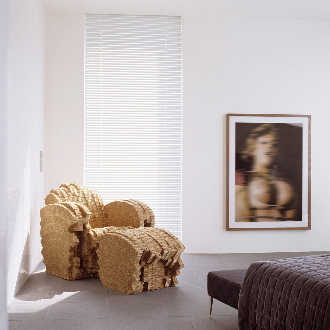 Designer armchair and ottoman made of corrugated cardboard in modern living room with artwork and blinds