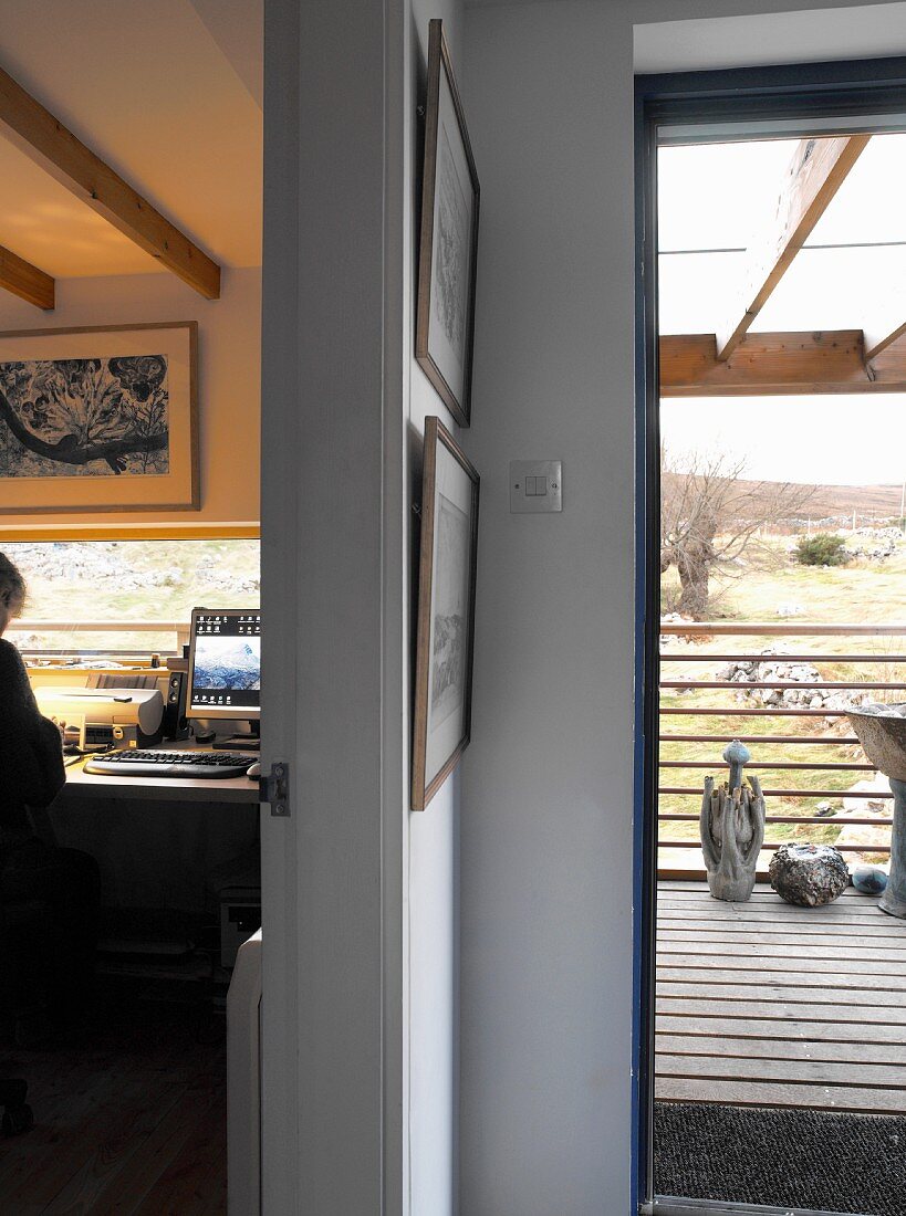 Blick auf karge Landschaft - Holzterrasse mit Skulpturen und schmales, liegendes Fenster in Homeoffice