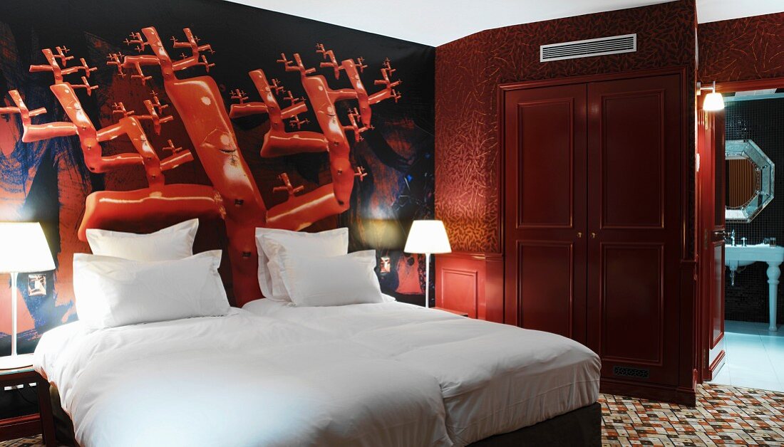 Bold, bright red mural behind snow-white bed in hotel room with ensuite bathroom