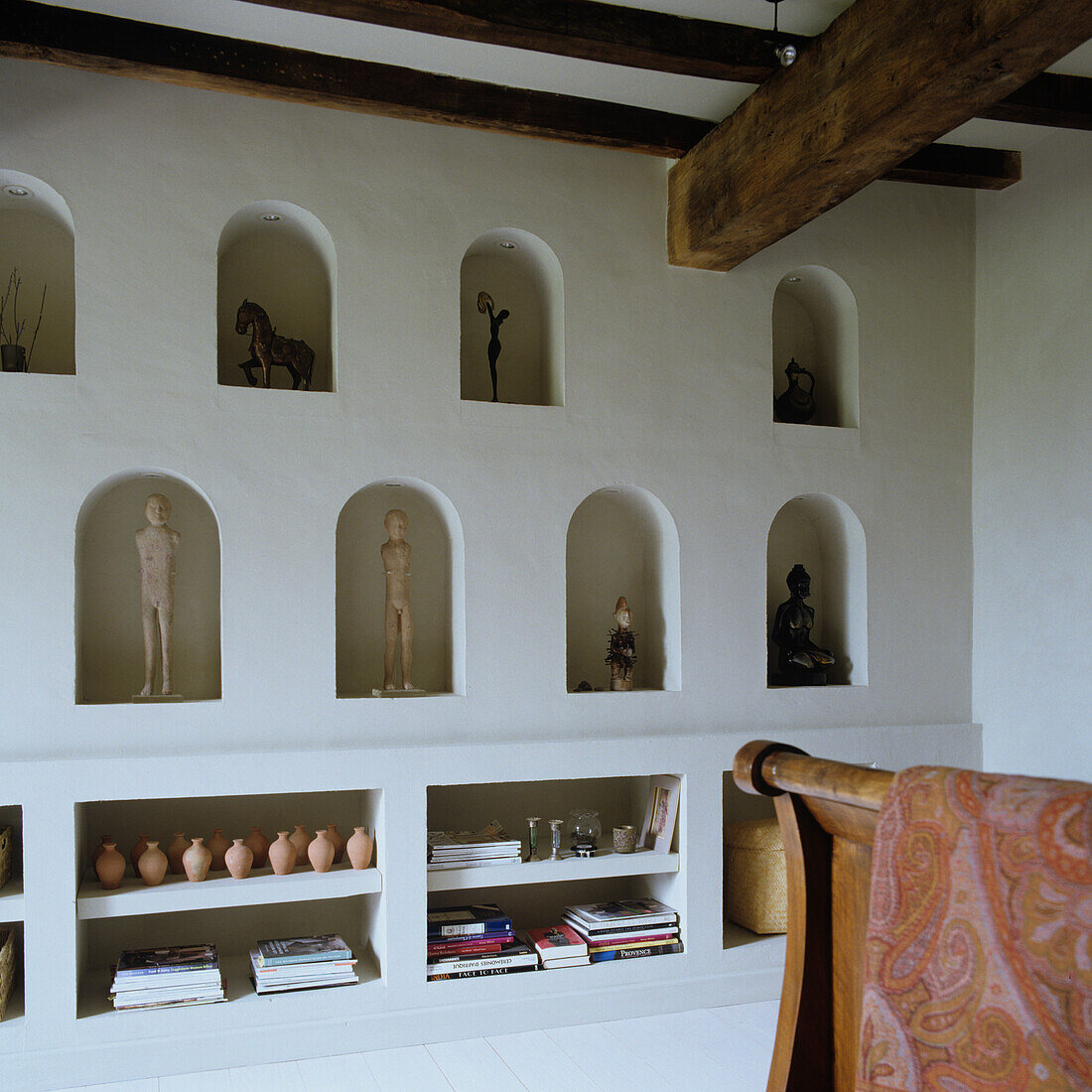 White wall with built-in wall niches and shelves, figures and wooden beamed ceiling