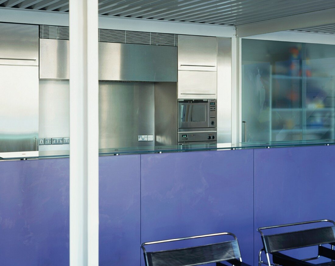 Lavender-coloured kitchen counter and black Bauhaus chairs in front of stainless steel kitchen units