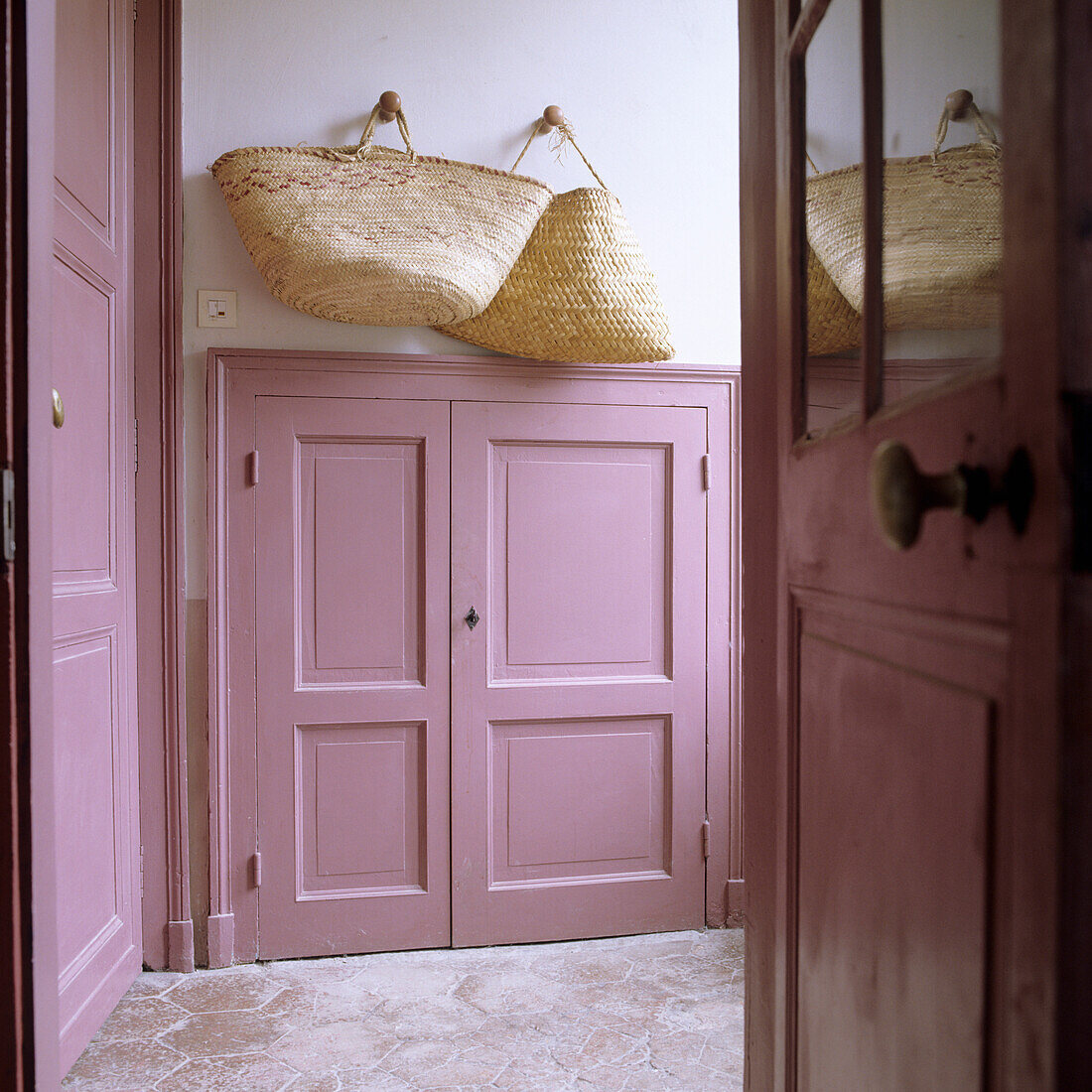 Hallway with door and cupboard in pink, woven baskets on the wall