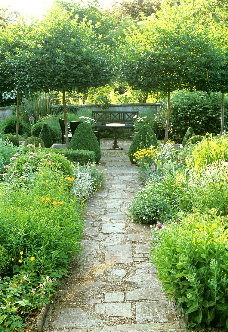 Gartenweg mit Natursteinplatten, umgeben von blühenden Staudenbeeten