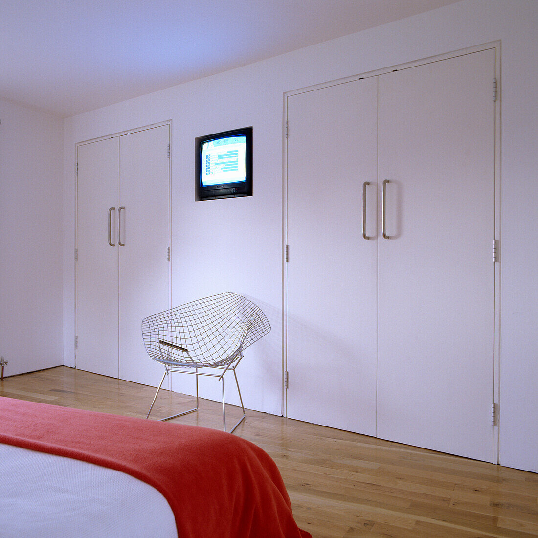 Minimalist bedroom with steel chair and red bedspread