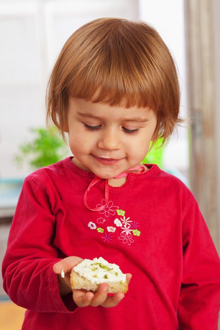 Kleines Mädchen hält Brotscheibe mit Hüttenkäse in der Händ