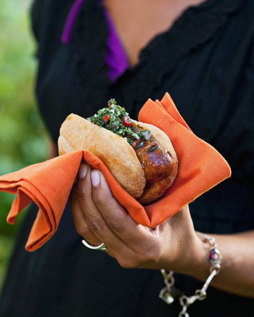 A woman holding a chimichurry hot dog
