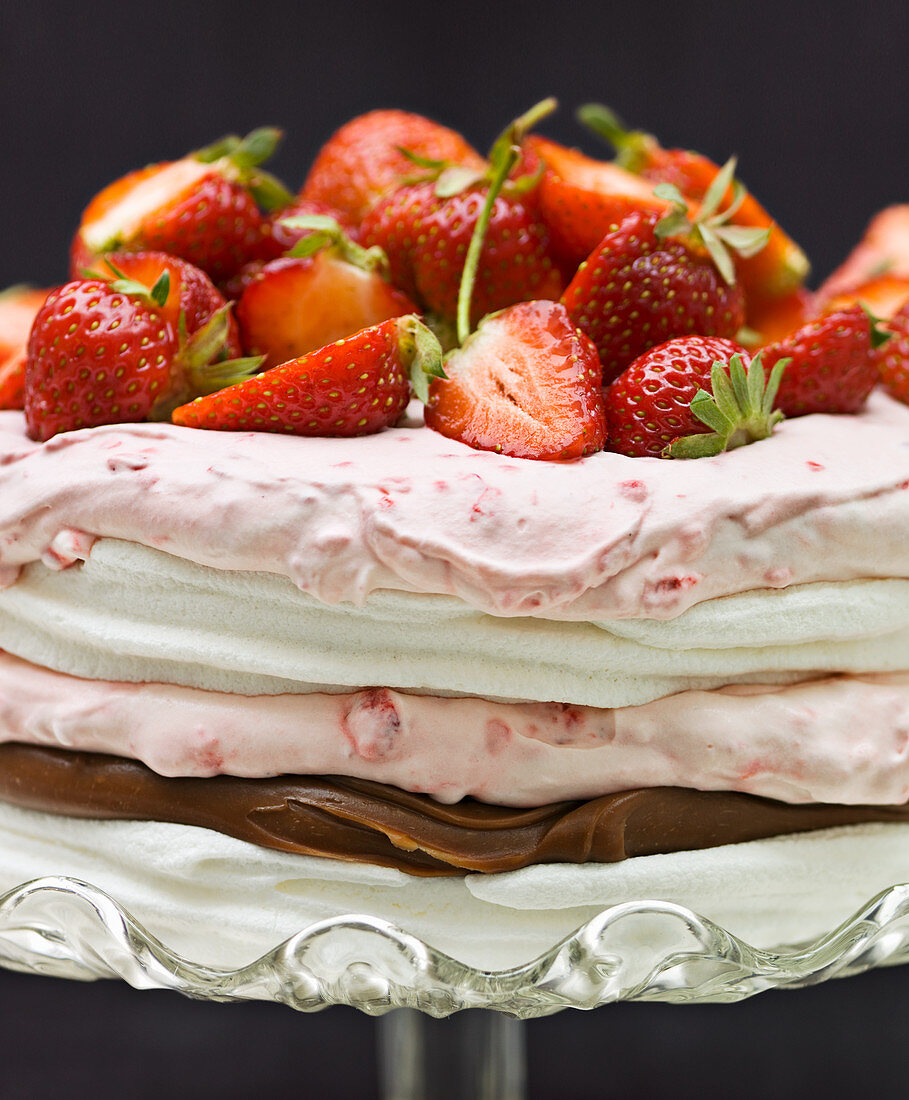 A layered meringue cake with raspberry cream, truffle cream and strawberries