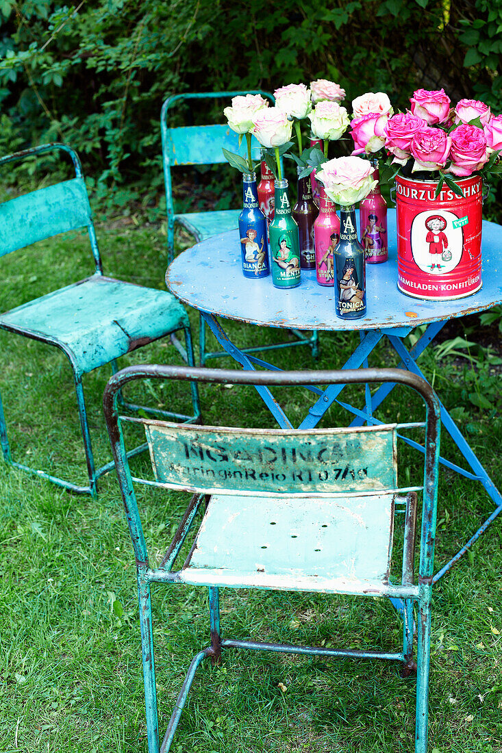 Retro-Gartentisch mit Rosen in Flaschenvasen und alten Metallstühlen