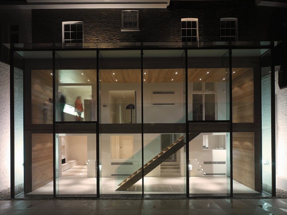 Zeitgenössischer Anbau mit Glasfront und Blick in beleuchteten mehrstöckigen Treppenraum