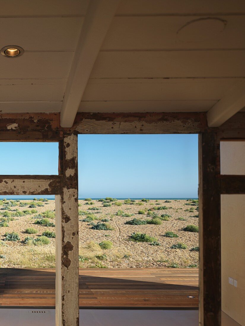 Blick durch verwitterte Holzkonstruktion einer alten Veranda über Strandlandschaft auf das Meer