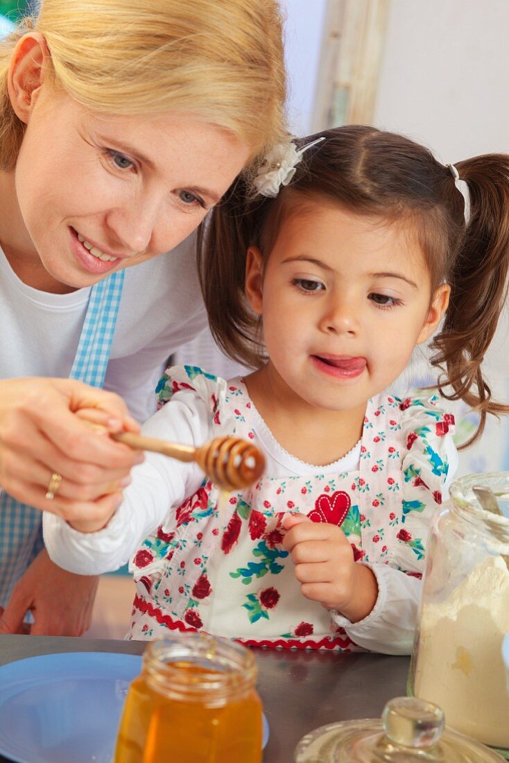Mutter & Tochter halten Honiglöffel über Honigglas