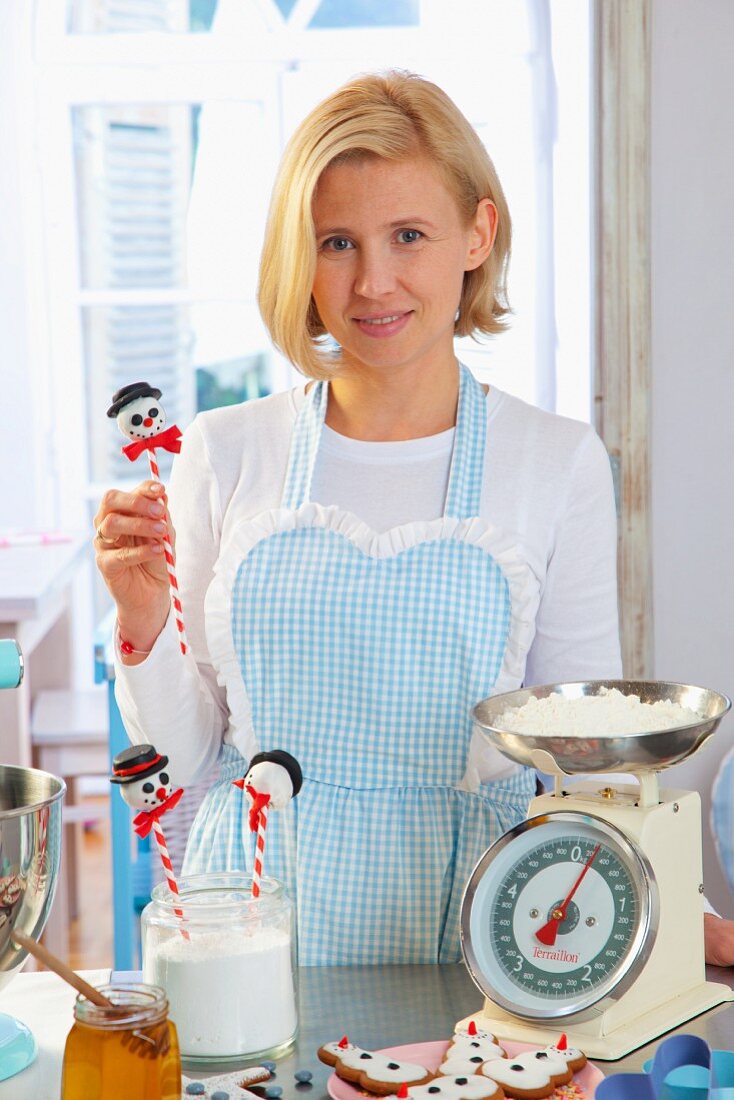 A woman with cake pops and ingredients for Christmas baking