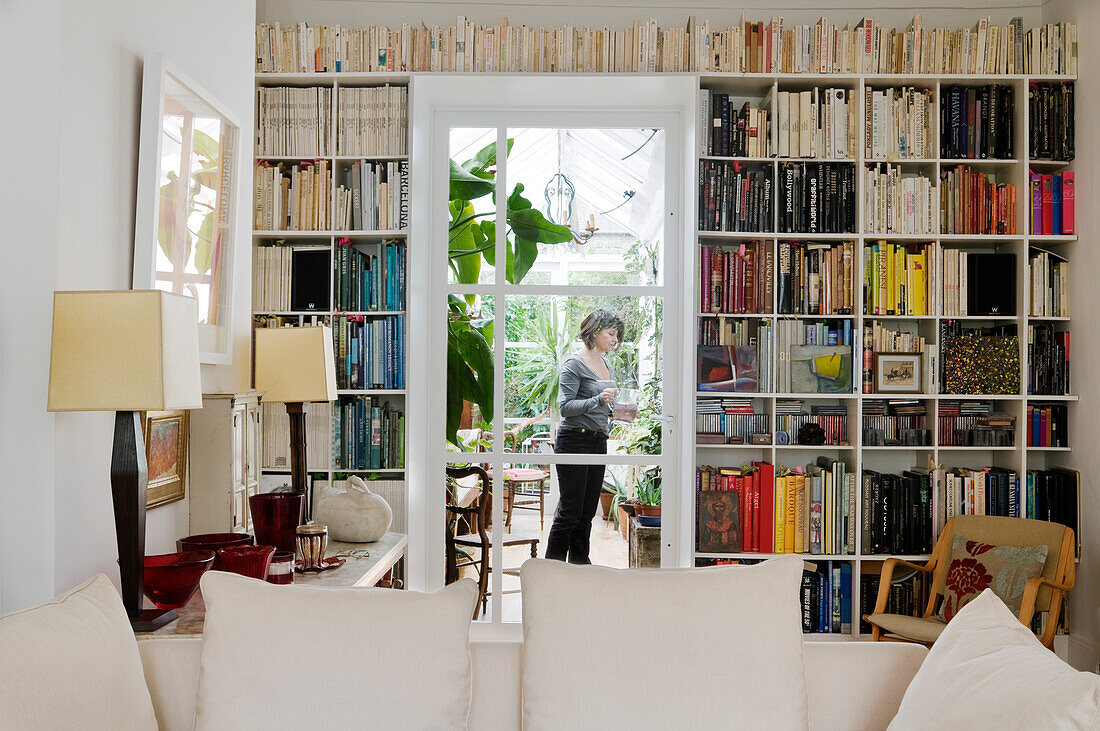 Wohnzimmer mit deckenhohem Bücherregal und Blick in den Wintergarten