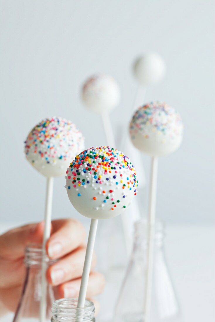 Hand Placing White Cake Pops with Colorful Sprinkles into Bottles