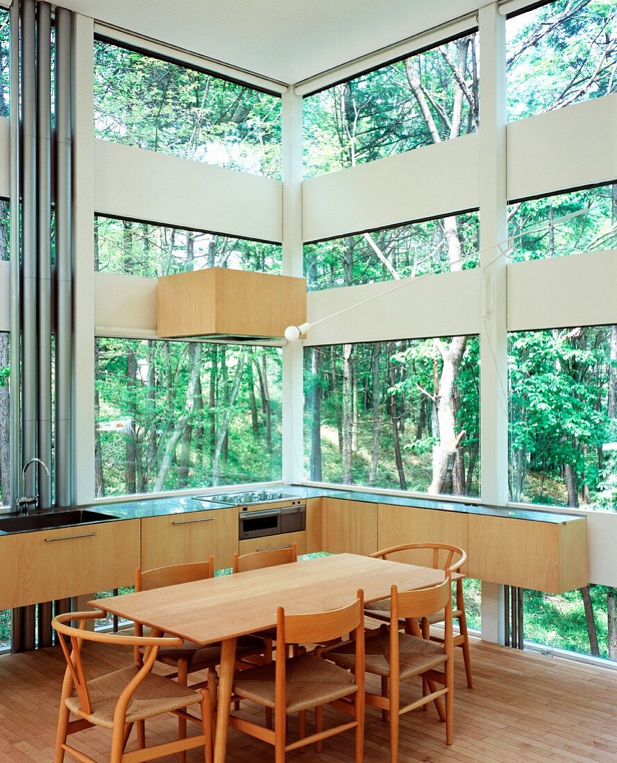 Kitchen with dining area in house made of glass and wood elements in forest