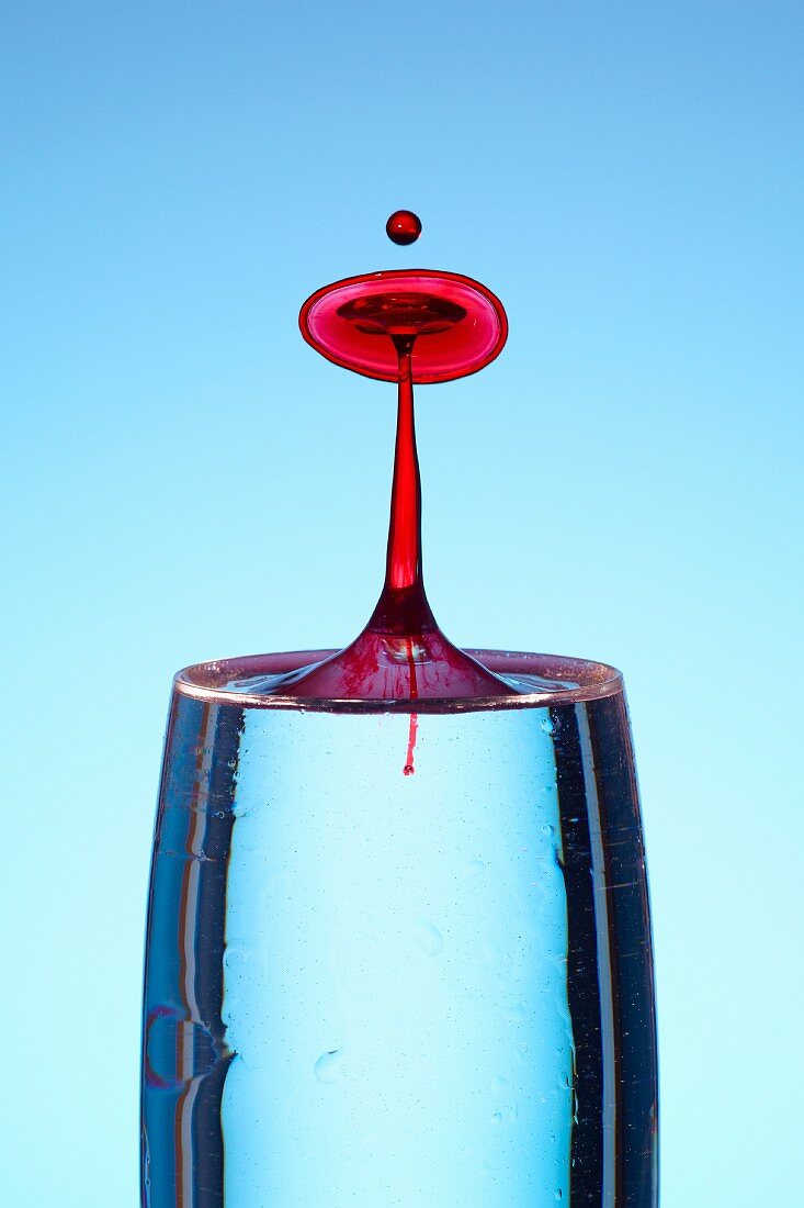 Red drops of water falling into a glass
