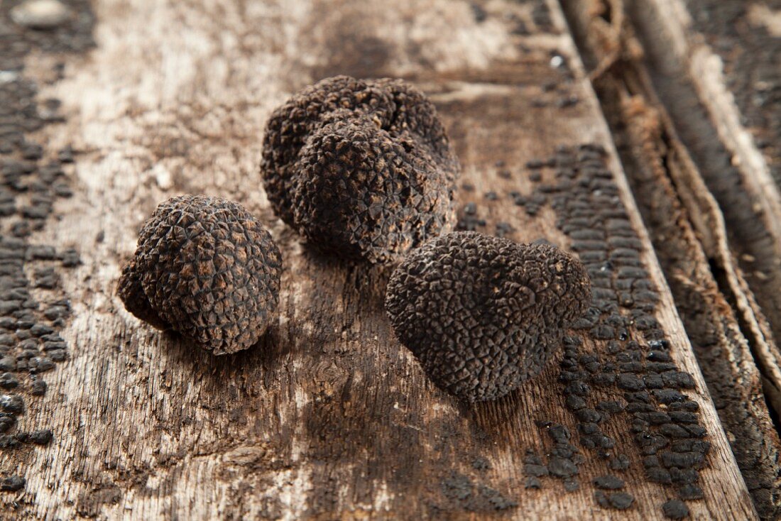 Three black truffles on a wooden surface
