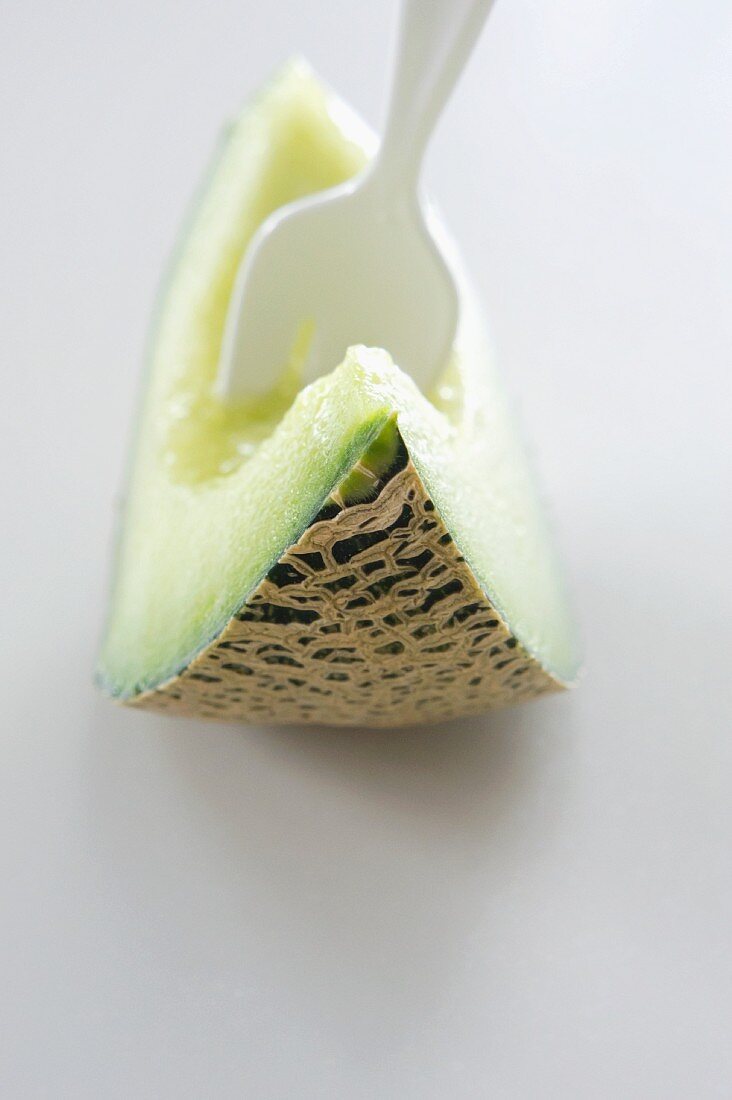 A fork stuck in a slice of honeydew melon