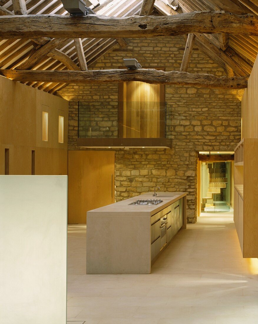 Im Designerstil ausgebauter offener Wohnraum mit freistehendem Küchenblock vor Natursteinwand