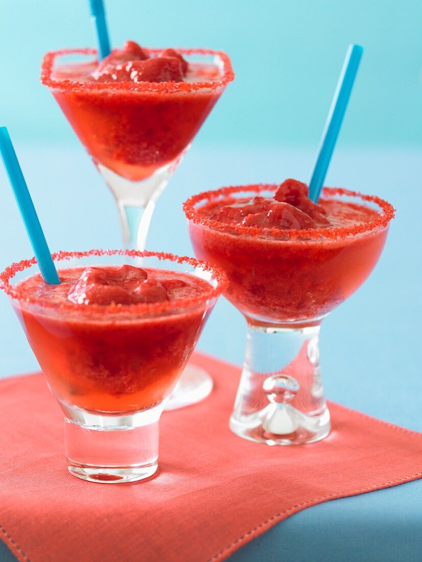 Three Fruity Red Cocktails with Blue Straws on a Red Napkin