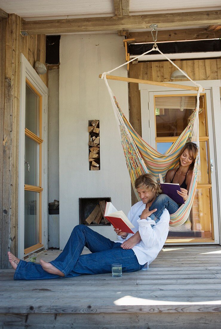 Couple reading on terrace: woman in hammock, man sitting on floor