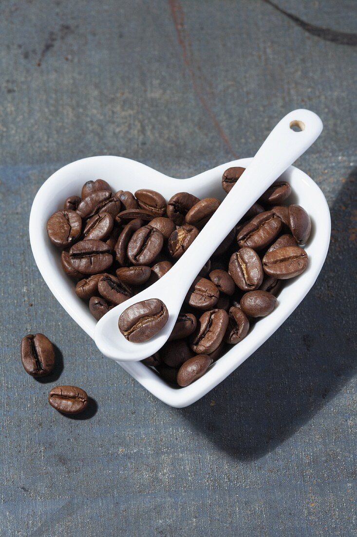 Coffee beans in a heart-shaped porcelain bowl with a porcelain spoon