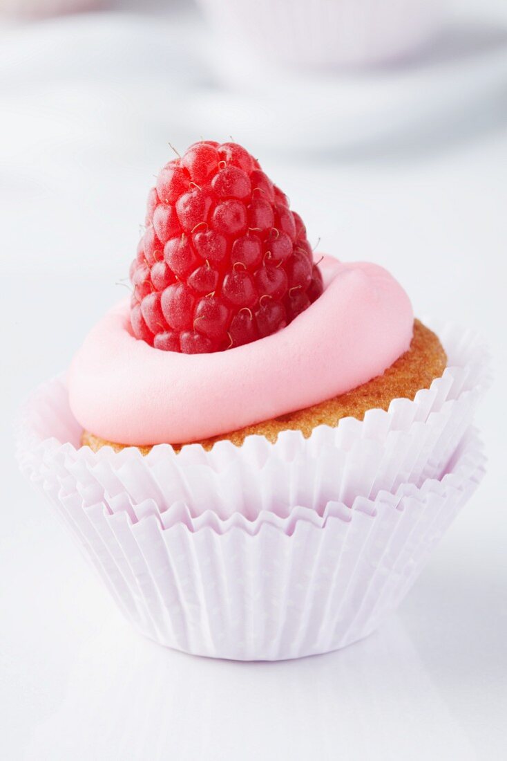 A mini muffin in a muffin case topped with raspberry mousse and a raspberry