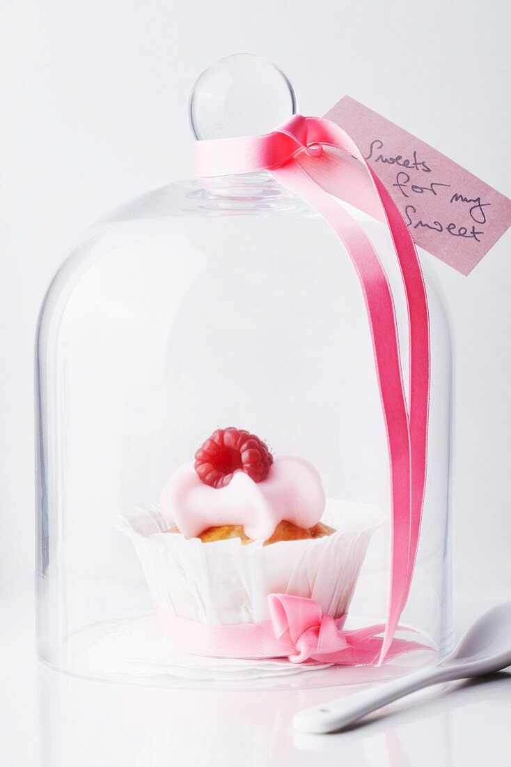 A raspberry muffin under a cloche decorated with a love letter and bow