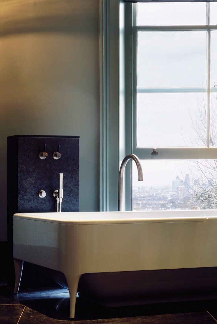 Extravagante gestylte Badewanne mit Designerarmatur vor Fenster mit Ausblick