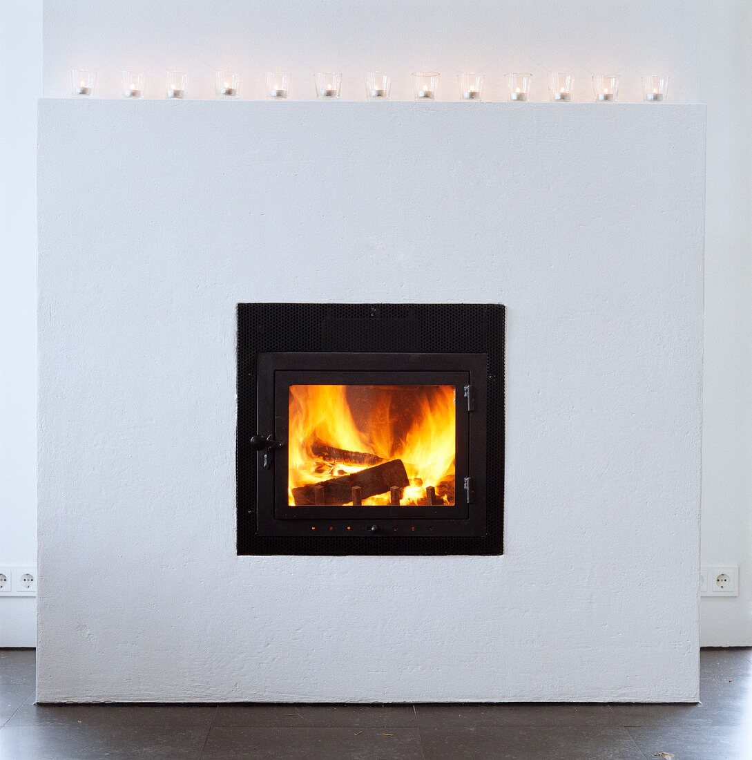 White, projecting masonry fireplace with tea light holders on mantelpiece and burning fire