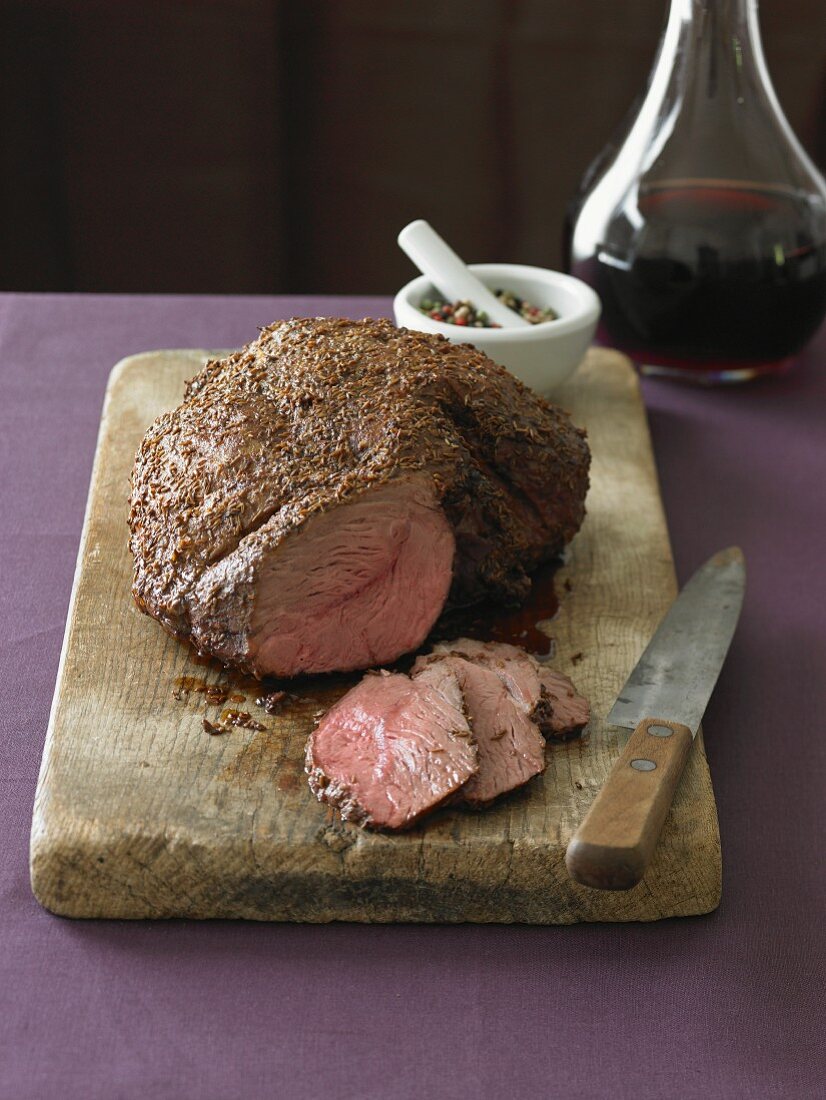 Leg of Lamb on a Cutting Board; Partially Sliced; Decanter of Wine