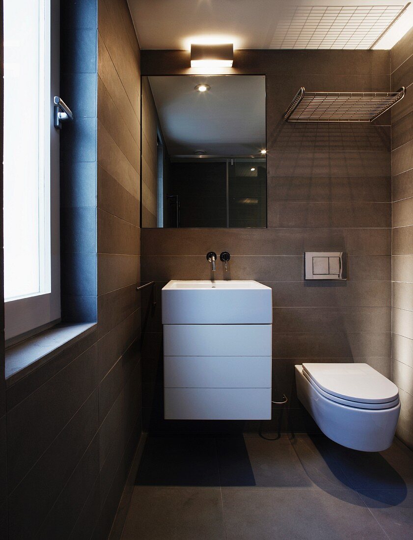 Grey tiled, designer bathroom with washstand and base unit next to wall-mounted toilet