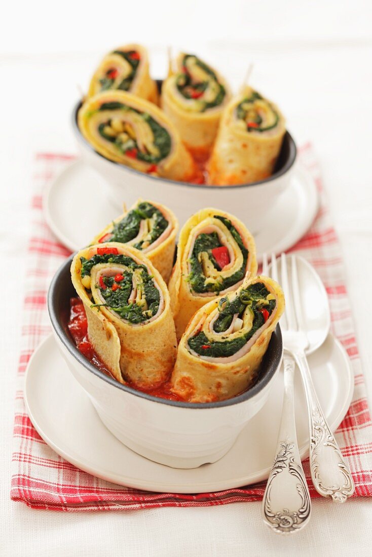 Pancake rolls filled with spinach and ham in tomato sauce