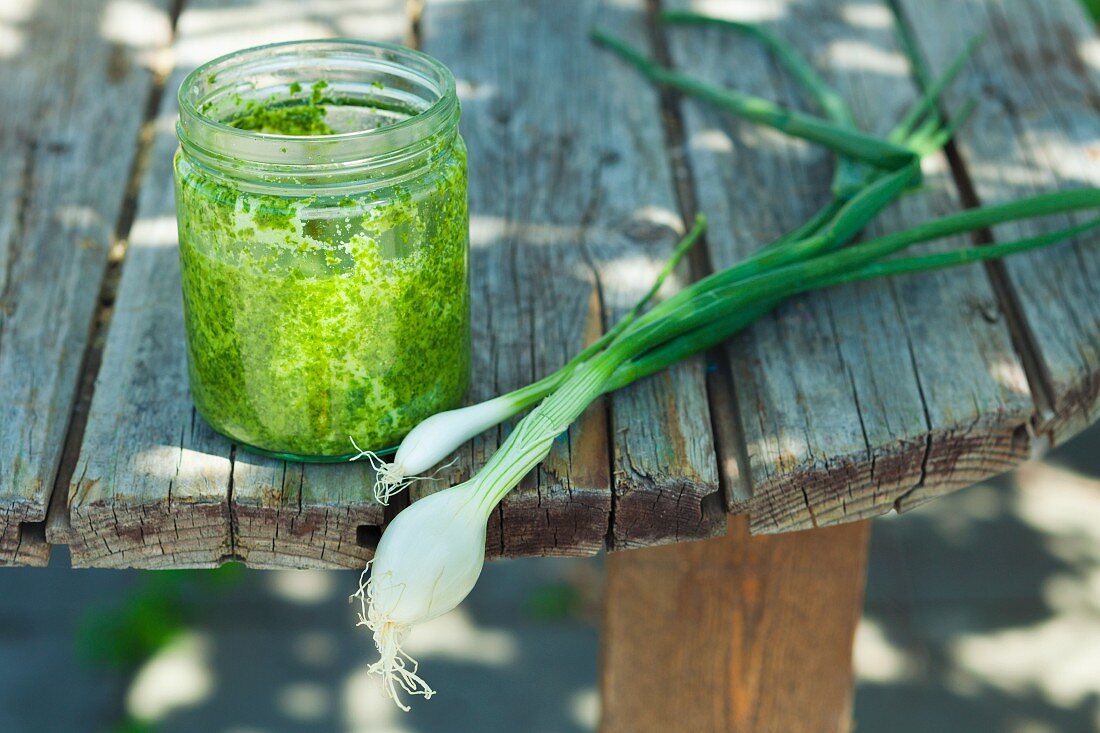 A jar of pesto and spring onions on a wooden table