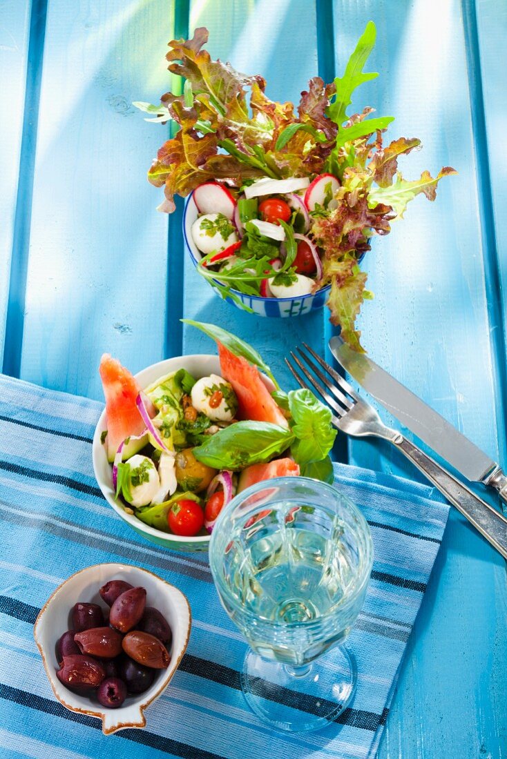 Two summer salads, olives and a glass of white wine