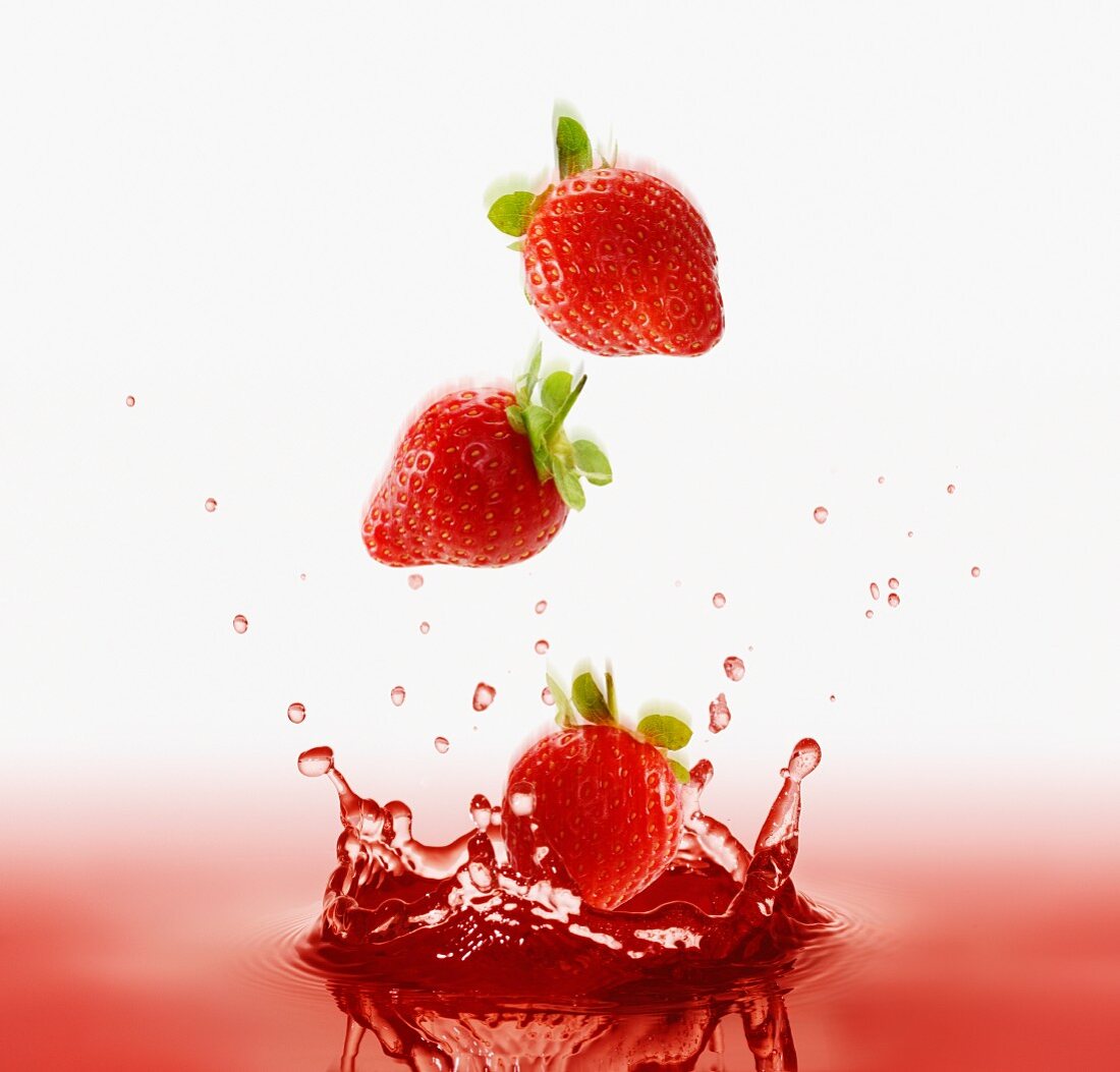 Erdbeeren fallen in roten Saft
