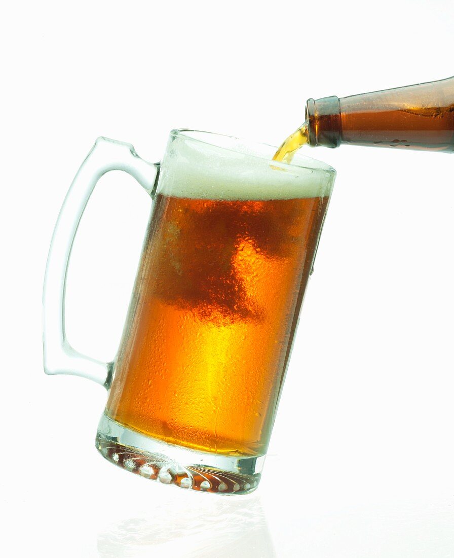 Beer pouring From a Bottle into a Glass Mug; White Background
