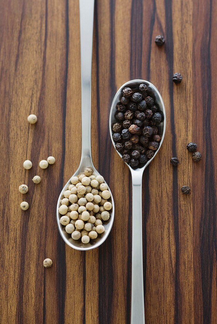 Black and white peppercorns on two spoons