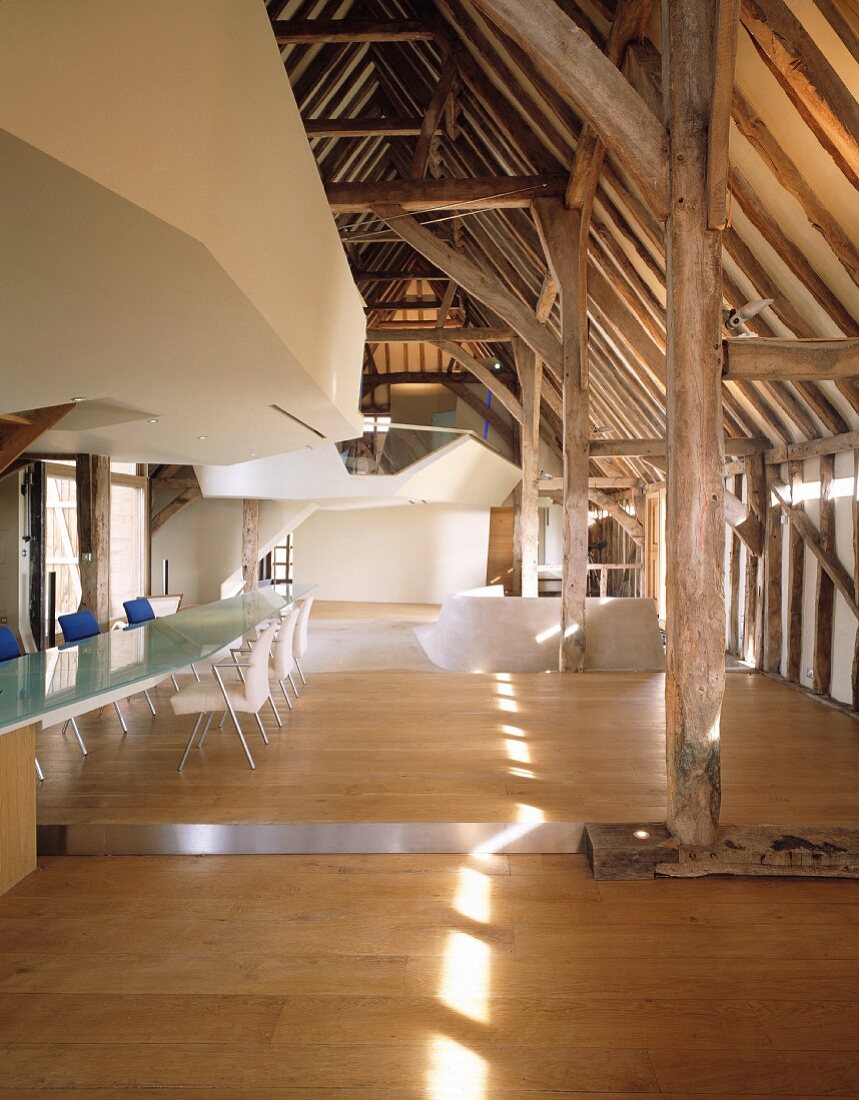 Roof structure in converted historic building with long, modern glass table next to glass wall