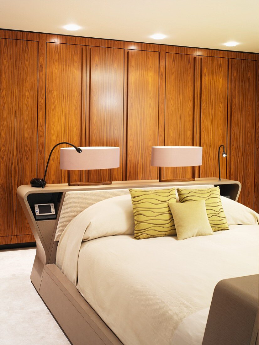 Bedside lamps on head of double bed in front of wooden fitted wardrobes