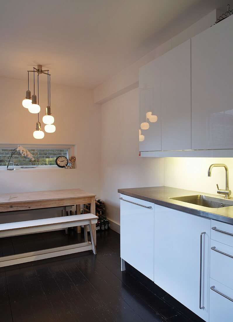 Retro-style light fitting with spherical shades and horizontal slit window above wooden table and benches in purist kitchen-dining room