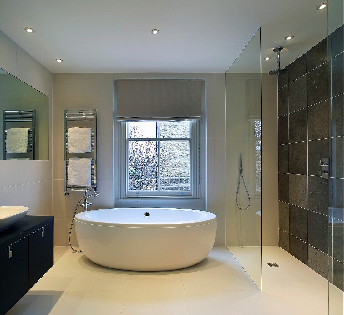 Free-standing, designer bathtub and floor-level shower with glass screen in modern bathroom
