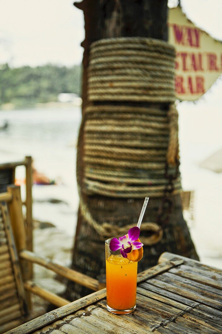 A glass of freshly squeezed orange juice with orchids on a beach (Thailand)