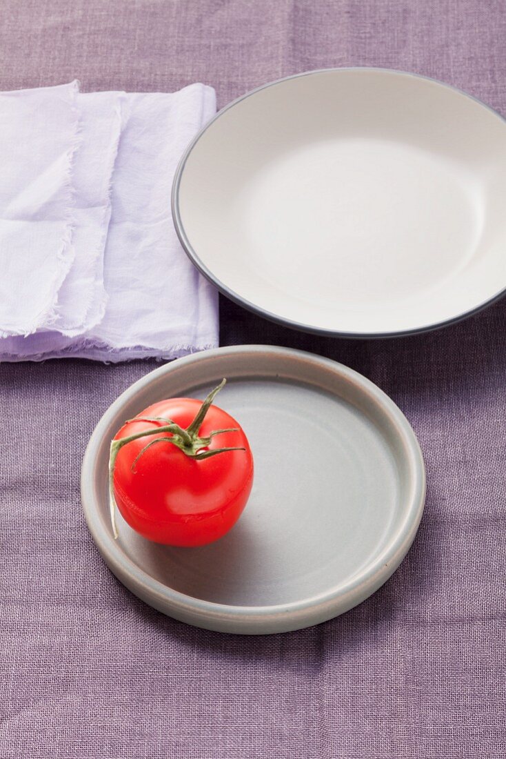 One tomato on a plate and an empty plate