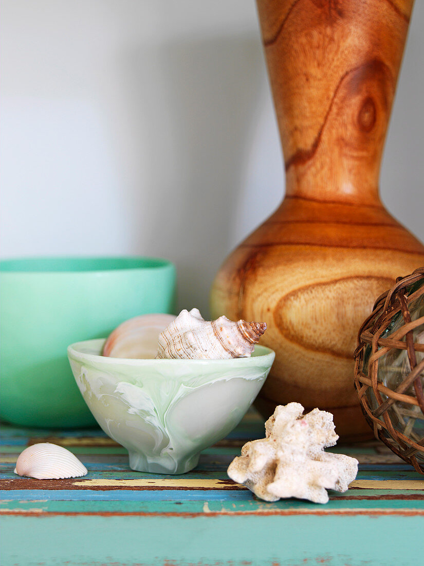 Muschel und Schneckenhäuser in Schale vor Vase aus Holz auf Ablage