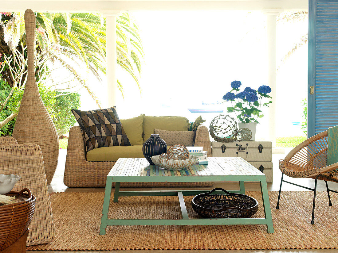 Colourful painted coffee table on sisal rug and rattan furniture in living room